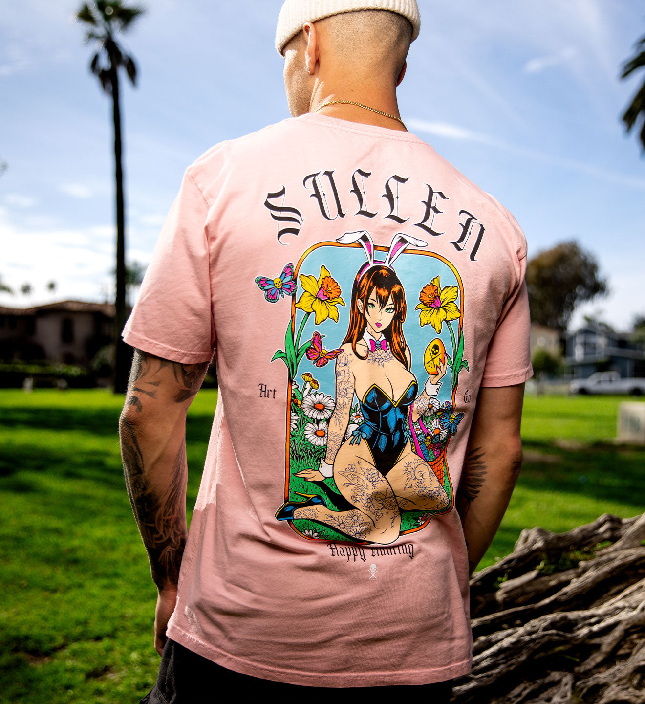 Person wearing a pink t-shirt with a colorful graphic design on the back, standing outdoors.